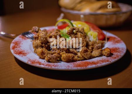 NAHAUFNAHME EINER TYPISCHEN SPANISCHEN CHOPITOS-MAHLZEIT MIT BEILAGEN IN EINEM ÜBER EINEM HOLZTISCH DEKORIERTEN TISCH MIT EINER GABEL AN DER SEITE Stockfoto