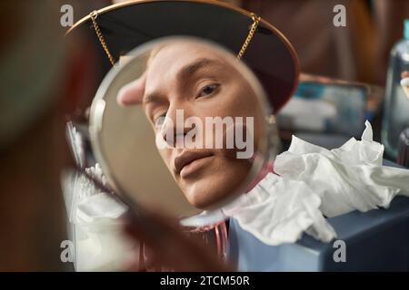 Nahaufnahme eines jungen Mannes, der in Spiegelreflektion Make-up macht und Foundation mit Puder aufträgt, Kopierraum Stockfoto