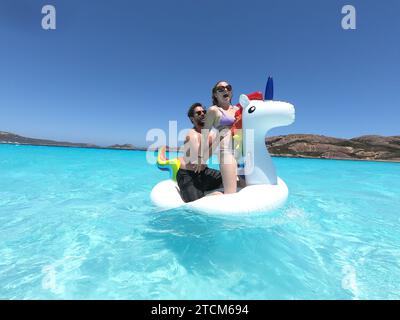 Ein lächelnder Mann und eine Frau, die einen sonnigen Tag auf einem aufblasbaren Schwan im Pool genießen Stockfoto