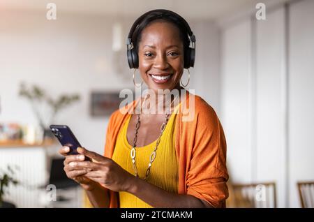 Frau hört Musik mit Kopfhörern, die mit ihrem Smartphone verbunden sind, im Wohnzimmer zu Hause Stockfoto