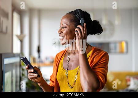 Frau hört Musik mit Kopfhörern, die mit ihrem Smartphone verbunden sind, im Wohnzimmer zu Hause Stockfoto