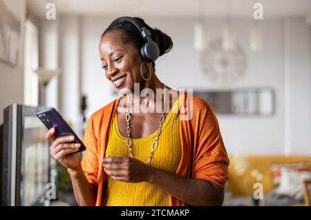 Frau hört Musik mit Kopfhörern, die mit ihrem Smartphone verbunden sind, im Wohnzimmer zu Hause Stockfoto