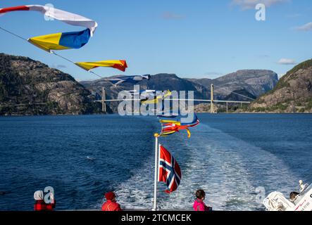 Pequeñas banderas en un barco ondeando al viento y el paisaje del Fiordo de la Luz o Lysefjord con el Puente Lysefjord y la estela del barco, Stavange Stockfoto