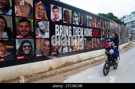 Tel Aviv, Israel. Dezember 2023. Am 13. Dezember 2023 reitet eine israelische Tochter an einer großen Plakatwand in Tel Aviv, Israel, vorbei, auf der alle Geiseln gezeigt werden, die von Hamas-Terroristen während ihrer Angriffe in Südisrael am 7. Oktober 2023 entführt wurden. Im Gazastreifen werden noch immer 137 Israelis als Geiseln festgehalten, während Israels Krieg gegen die Hamas im dritten Monat stattfindet. Foto von Jim Hollander/UPI Credit: UPI/Alamy Live News Stockfoto