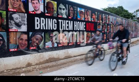 Tel Aviv, Israel. Dezember 2023. Ein Israelis und sein Sohn fahren am 13. Dezember 2023 mit dem Fahrrad an einer großen Plakatwand in Tel Aviv, Israel, vorbei, auf der alle Geiseln gezeigt werden, die von Hamas-Terroristen während ihrer Angriffe in Südisrael am 7. Oktober 2023 entführt wurden. Im Gazastreifen werden noch immer 137 Israelis als Geiseln festgehalten, während Israels Krieg gegen die Hamas im dritten Monat stattfindet. Foto von Jim Hollander/UPI Credit: UPI/Alamy Live News Stockfoto