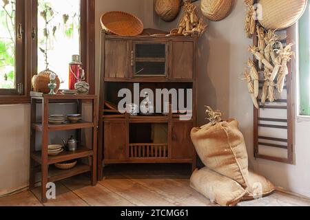 Innenraum der vietnamesischen Küche mit Porzellanvase, Aluminiumkessel, blauer Porzellanplatte, Rattanuntersetzer, Öllampe, Vintage Thermosflasche in Stockfoto