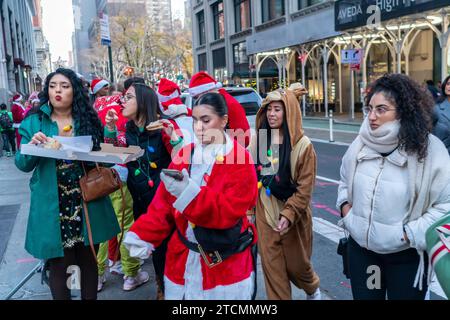 Hunderte von Santas, begleitet von ihren Helfern und einigen frechen Elfen, warten online, um die Smith Bar im Nomad-Viertel in Manhattan in New York während des jährlichen Kneipenbummels SantaCon am Samstag, den 19. Dezember 2023, zu betreten. Die SantaCon, in erster Linie ein Kneipenbummel in Weihnachtskostümen und anderen Weihnachtskostümen, zieht Maskierer an, die von Bar zu Bar gehen. (© Richard B. Levine) Stockfoto