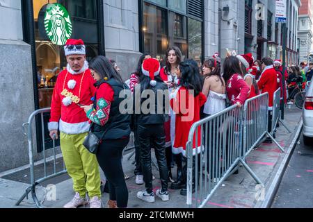 Hunderte von Santas, begleitet von ihren Helfern und einigen frechen Elfen, warten online, um die Smith Bar im Nomad-Viertel in Manhattan in New York während des jährlichen Kneipenbummels SantaCon am Samstag, den 19. Dezember 2023, zu betreten. Die SantaCon, in erster Linie ein Kneipenbummel in Weihnachtskostümen und anderen Weihnachtskostümen, zieht Maskierer an, die von Bar zu Bar gehen. (© Richard B. Levine) Stockfoto