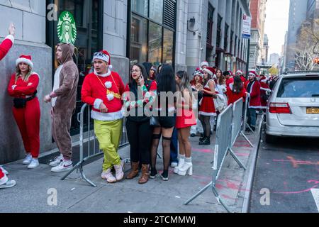 Hunderte von Santas, begleitet von ihren Helfern und einigen frechen Elfen, warten online, um die Smith Bar im Nomad-Viertel in Manhattan in New York während des jährlichen Kneipenbummels SantaCon am Samstag, den 19. Dezember 2023, zu betreten. Die SantaCon, in erster Linie ein Kneipenbummel in Weihnachtskostümen und anderen Weihnachtskostümen, zieht Maskierer an, die von Bar zu Bar gehen. (© Richard B. Levine) Stockfoto