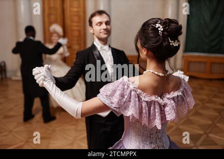 Rückansicht einer jungen Dame, die Ballkleid trägt und Walzer mit Gentleman im Palast tanzt Stockfoto