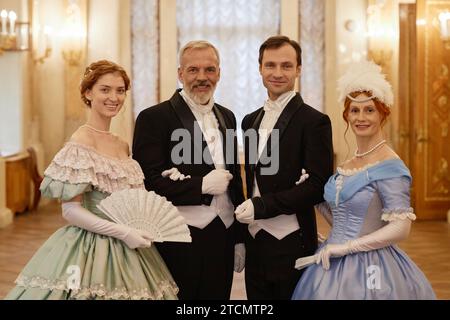Verschiedene Gruppen von Menschen in historischen Kostümen, die auf die Kamera im Palastsaal blicken Stockfoto