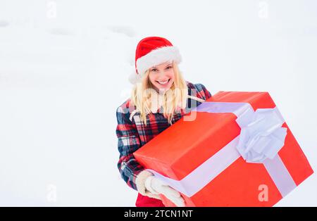 Weihnachtsmädchen mit einem großen Geschenk. Verrücktes Weihnachtsmädchen schiebt ein großes Geschenk auf Schnee Winter Hintergrund. Frohe Weihnachten und frohe Feiertage. Stockfoto