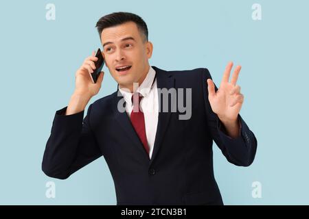 Hübscher Geschäftsmann mit Handy, der Hand auf blauem Hintergrund winkt Stockfoto