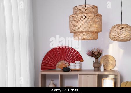 Holzschrank mit rotem Ventilator, Teekanne und getrockneten Blumen im Wohnzimmer. Chinesisches Neujahrsfest Stockfoto