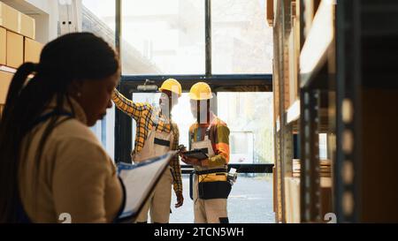 Team von Männern, die am Lagerbestand im Lager arbeiten, Warencodes mit Scanner scannen und die Zwischenablage überprüfen. Zwei Mitarbeiter des Depots verwenden ein Tablet, um Barcodes zu scannen. Stativaufnahme. Stockfoto
