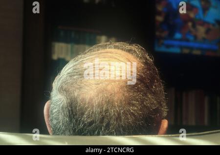 Rückansicht Kopf des Glatzköpfigen Mannes, der fern sieht. Älterer Rentner, der allein zu Hause in einem verdunkelten Zimmer fernsieht. Ruhestand, Sozialversicherung USA Stockfoto