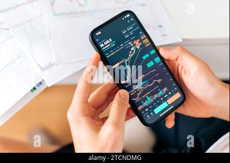 Nahaufnahme eines Smartphones in männlichen Händen, mit Index-Diagramm für Handelsdaten auf dem Bildschirm, App-Analysen für Mobiltelefone für den Kryptowährungsmarkt. Online-Handel Stockfoto