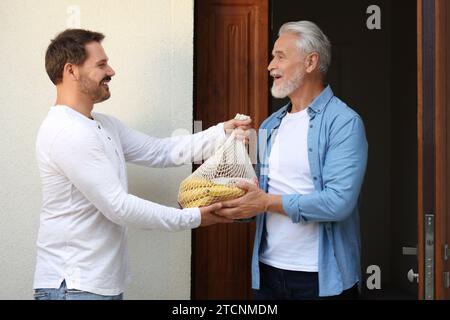 Mann mit Netztüte mit Produkten, die seinem Seniorennachbarn im Freien helfen Stockfoto