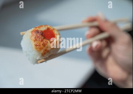 Eine Frau hält eine Rolle mit Stäbchen. Nahaufnahme der Hand einer Frau mit japanischem Essen. Stockfoto