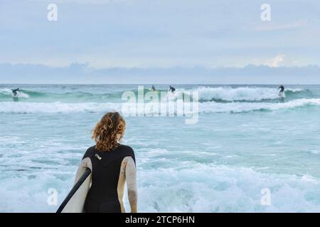 Sydney, NSW, Australien - 02. Dezember 2023: Eine Surferin schaut an einem windigen, bewölkten Samstagmorgen am Bondi Beach auf die Wellen Stockfoto