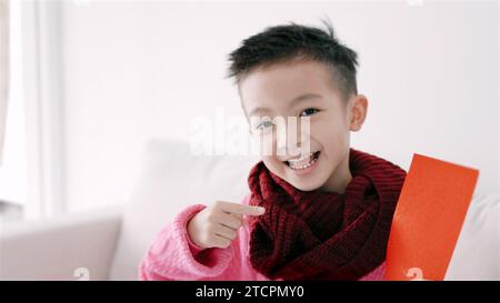 Glücklicher asiatischer Junge, der roten Umschlag zeigt und hält. Happy Chinese New Year Konzept. Stockfoto