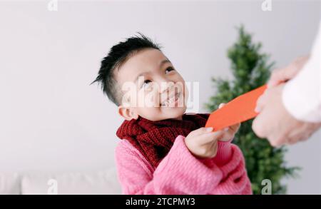 Ein glücklicher asiatischer kleiner Junge, der einen roten Umschlag erhält und das chinesische Neujahr feiert Stockfoto