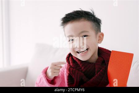 Glücklicher asiatischer Junge, der roten Umschlag zeigt und hält. Happy Chinese New Year Konzept. Stockfoto