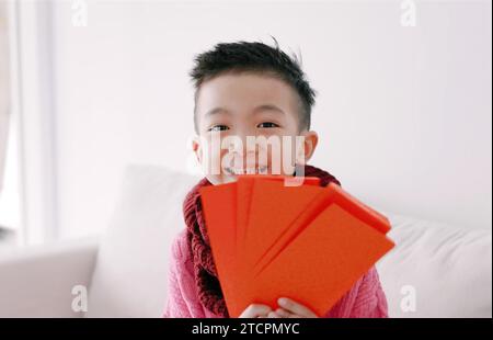 Glücklicher asiatischer Junge, der roten Umschlag zeigt und hält. Happy Chinese New Year Konzept. Stockfoto