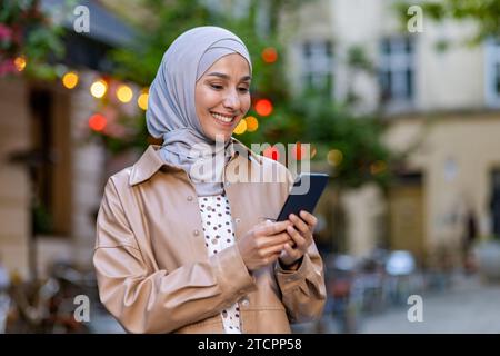 Eine junge muslimische Frau in einem Hijab steht auf der Straße und hält ein Telefon in der Hand, schreibt SMS, läuft durch die Stadt, macht Urlaub. Stockfoto