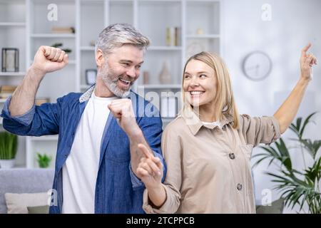 Glückliches Seniorenpaar tanzt im älteren Wohnzimmer, glücklicher Ehemann und Frau, Familienwerte. Stockfoto