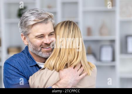 Ältere Ehemann und Ehefrau umarmen sich im hellen Wohnzimmer zu Hause, warme Familienbeziehung. Stockfoto