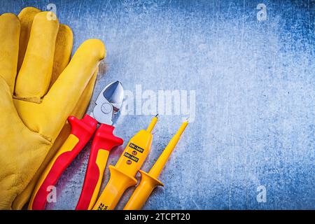 Gelbes elektrisches Prüfgerät Sicherheitshandschuhe Rote Zange auf metallischem Hintergrund Elektrizitätskonzept Stockfoto