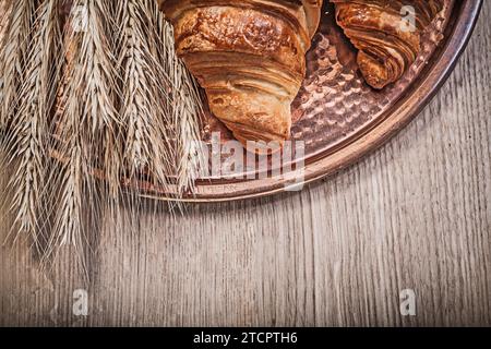 Zusammensetzung von Weizenroggenohren frisch gebackene Croissants Kupfertablett auf Holzbrett Stockfoto