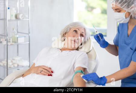 Weibliche Ärztin, die der schläfrigen, müden alten Frau in der Klinik eine Injektion gibt. Stockfoto