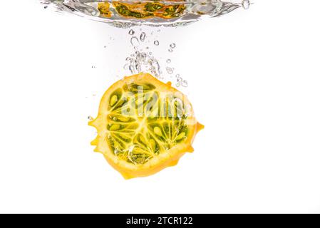 Kiwano oder Horned Melon (Cucumis metuliferus) Spritzer in einer Hälfte auf weißem Hintergrund unter Wasser isolierte Nahaufnahme geschnitten Stockfoto