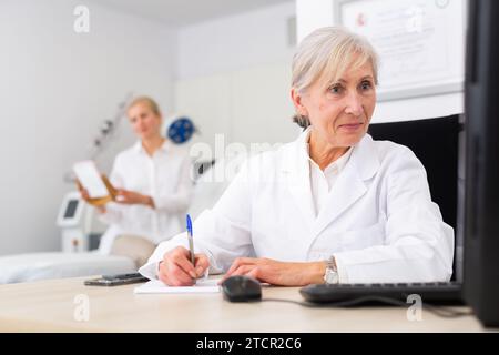 Seniordermatologin schreibt Notizen während des Termins Stockfoto