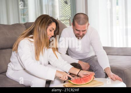 Eine dreiköpfige Familie isst eine köstliche Wassermelone im Wohnzimmer Stockfoto