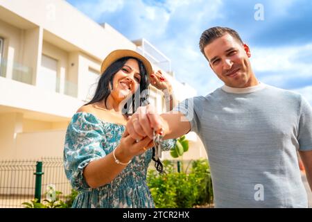 Glückliches Paar, das die Schlüssel eines neuen Hauses vor der neuen Residenz zeigt Stockfoto