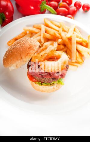 Klassisches amerikanisches Hamburger-Sandwich mit Zwiebelringen und Pommes frites, mit frischem Gemüse IM Hintergrund, MEHR LECKERE SPEISEN IM PORTFOLIO Stockfoto