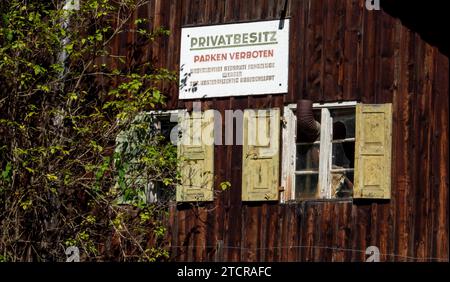 21.09.2023, Deutschland, auf dem Foto ein altes sanierungsbedürftiges Holzhaus mit zwei Holzfenstern sowie den dazugehörigen Fensterläden, aus dem rechten Doppelfenster ragt ein Ofenrohr als Schornstein heraus, darüber sich ein Schild mit der Aufschrift PRIVATBESITZ PARKEN VERBOTEN UNBERECHTIGT GEPARKTE FAHRZEUGE WERDEN SOF. KOSTENPFLICHTIG ABGESCHLEPPT *** 21 09 2023, Deutschland, auf dem Foto ein altes, renovierungsbedürftiges Holzhaus mit zwei Holzfenstern und den dazugehörigen Fensterläden, aus dem rechten Doppelfenster ragt als Schornstein ein Ofenrohr hervor, darüber ein Schild mit der Inschrift Stockfoto