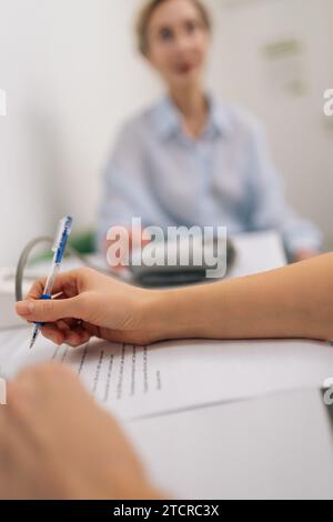 Close-up-Hände einer nicht erkennbaren Ärztin, die Notizen auf dem Klemmbrett macht, die Patientin mittleren Alters berät und die medizinischen Ergebnisse erklärt Stockfoto