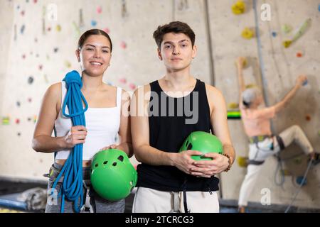Motivierte, sportliche Jugendliche, Mann und Frau, die mit Spezialausrüstung stehen, bevor sie im Vergnügungszentrum die Boulderwand hochklettern Stockfoto