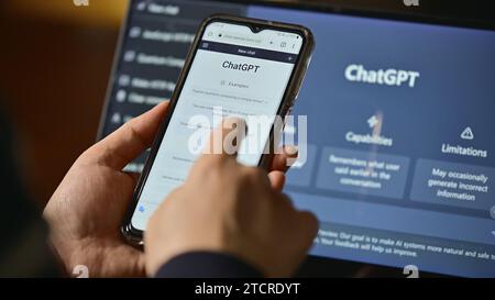 Seoul, Südkorea - Februar 2023 : Computerbildschirm mit ChatGPT-Website und Person, die ihr Mobiltelefon benutzt, um Fragen an ChatGPT zu stellen Stockfoto
