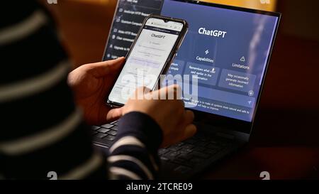 Seoul, Südkorea - Februar 2023 : Computerbildschirm mit ChatGPT-Website und Person, die ihr Mobiltelefon benutzt, um Fragen an ChatGPT zu stellen Stockfoto