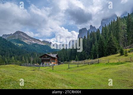 Eingebettet im Val di Funes, steht eine Holzhütte vor der Kulisse der Dolomiten, umgeben von üppigen grünen Weiden, ein ruhiger alpiner Rückzugsort Stockfoto