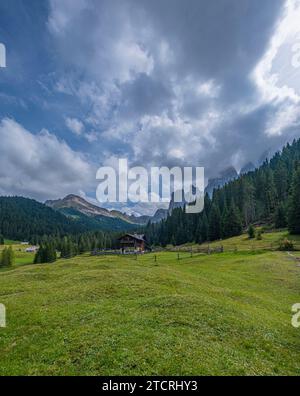 Eingebettet im Val di Funes, steht eine Holzhütte vor der Kulisse der Dolomiten, umgeben von üppigen grünen Weiden, ein ruhiger alpiner Rückzugsort Stockfoto