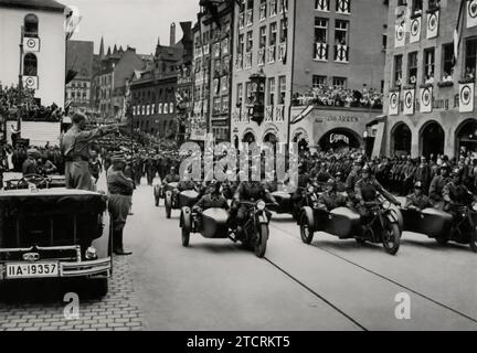 Beim Reichsparteitag 1935 sieht man Adolf Hitler in seinem offenen Auto stehen und die motorisierten SA-Sturmabteilung grüßen. Dieses Bild fängt einen Moment der Interaktion zwischen Hitler und der SA ein und betont die Rolle der Motorisierung im NS-Militärapparat. Hitlers Gruß aus dem Auto, ein Symbol für seine Führung und die Modernisierungsbemühungen des Regimes, unterstreicht die Bedeutung der SA für die Demonstration der Stärke und Einheit der Partei während dieser großen, stark choreografierten Ereignisse. Stockfoto