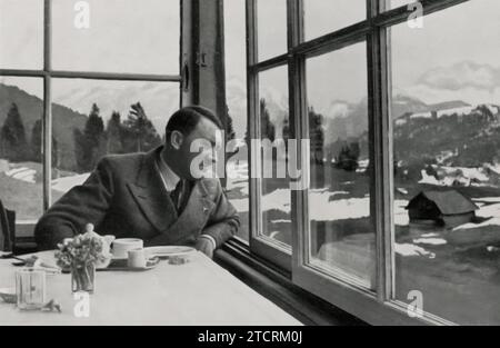 Adolf Hitler wird an einem Esstisch auf der G'schwandner Alm bei Garmisch gefangen genommen und blickt aus einem Fenster in Richtung Berge. Dieses Bild zeigt einen kontemplativen Moment und unterstreicht die landschaftliche Schönheit der umliegenden Landschaft. Die Umgebung, abseits der üblichen politischen Kulisse, soll eine entspanntere und reflektierendere Seite Hitlers darstellen, eine Abkehr von seinem öffentlichen und politischen Leben. Stockfoto