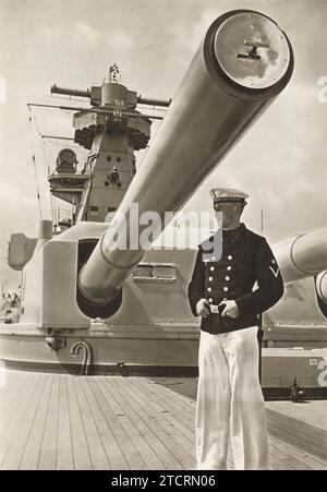 In diesem Bild steht eine deutsche Marine, die als Vormann auf der Brücke identifiziert wurde, vor dem massiven hinteren Geschützturm an Bord des gepanzerten Schiffes Admiral Graf Spee. Die Anwesenheit eines so hochrangigen Offiziers auf der Brücke unterstreicht die strategische Bedeutung dieser Position für die Überwachung der Marineoperationen. Der Admiral Graf Spee, bekannt für seine bedeutende Rolle in der Kriegsmarine während des Zweiten Weltkriegs, war mit mächtiger Artillerie ausgestattet, wie der imposante Turm veranschaulicht Stockfoto
