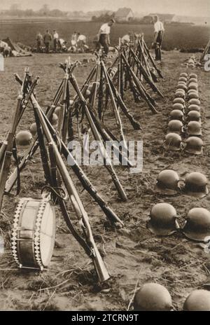 Die Ausrüstung der deutschen Soldaten wird präzise ausgestellt und zeigt ihre akribische Liebe zum Detail. Im Hintergrund stehen Soldaten, während im Vordergrund ihre Gewehre ordentlich gestapelt sind, um eine tipi-ähnliche Struktur zu bilden. Diese Anordnung demonstriert nicht nur die Ordnung und Disziplin, die dem militärischen Leben innewohnt, sondern symbolisiert auch die Einheit und Bereitschaft der Truppen. Stockfoto